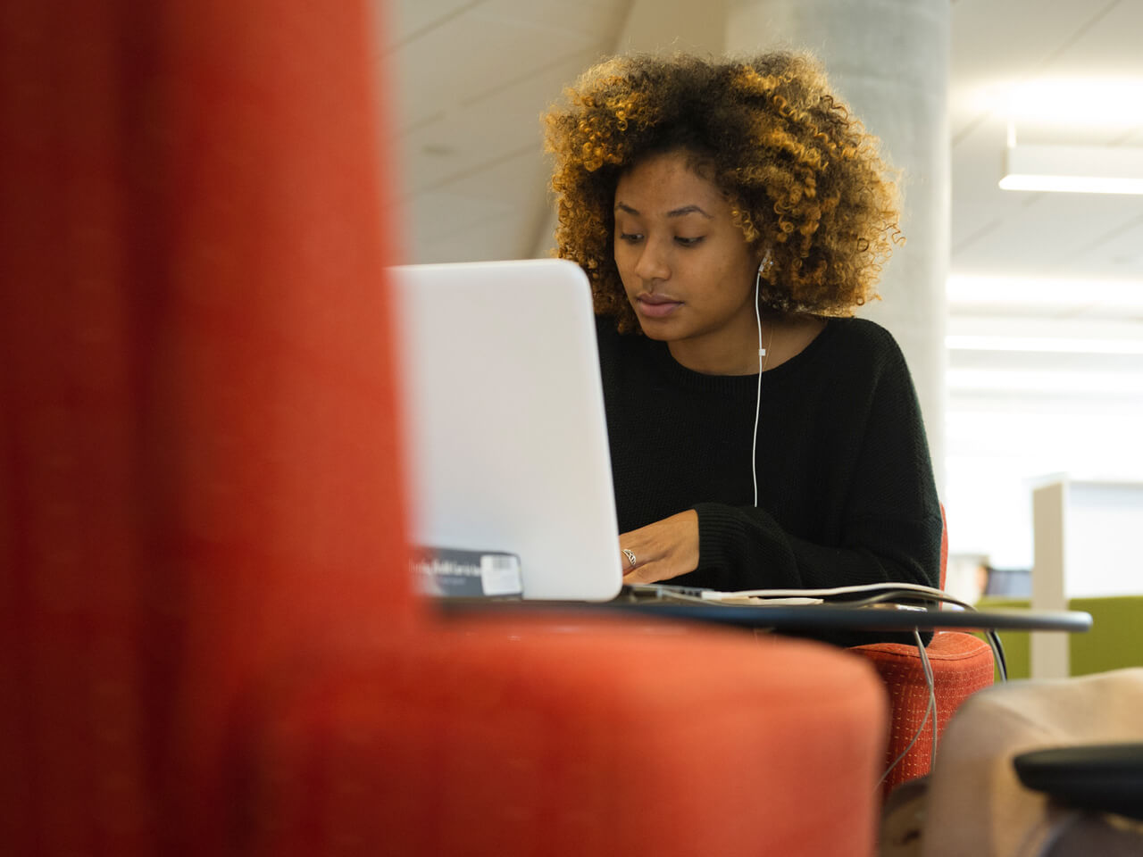 Student working on a laptop sitting on a red chair